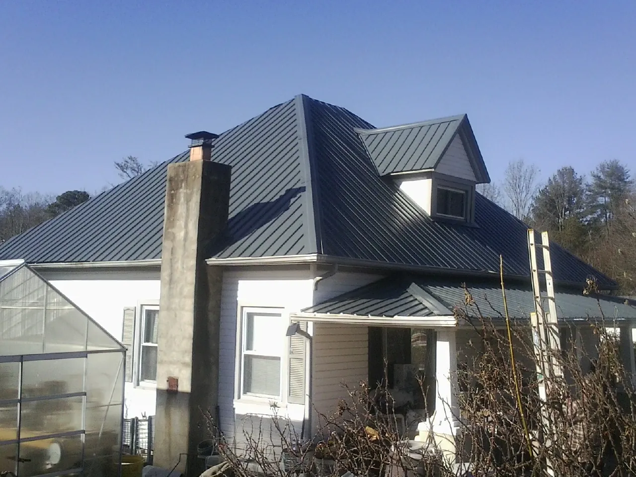 Dark blue standing seam metal roof on a white farmhouse with dormer — Slate & Tile Roof Repair by Roofing Brothers in Little Cedar