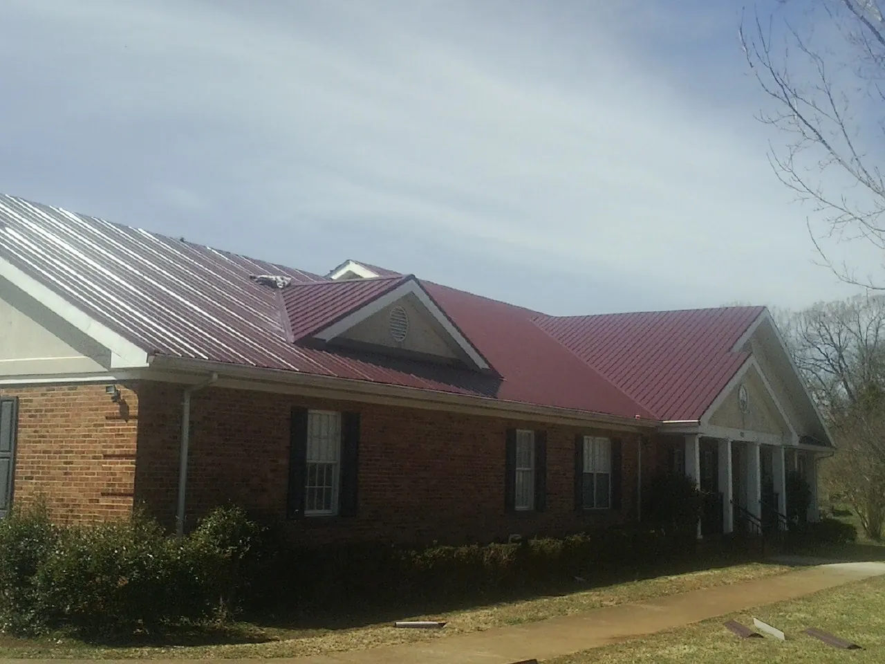 Red metal roof with gabled entries on a long brick building, from a Hail Damage Roof Repair job in Little Cedar
