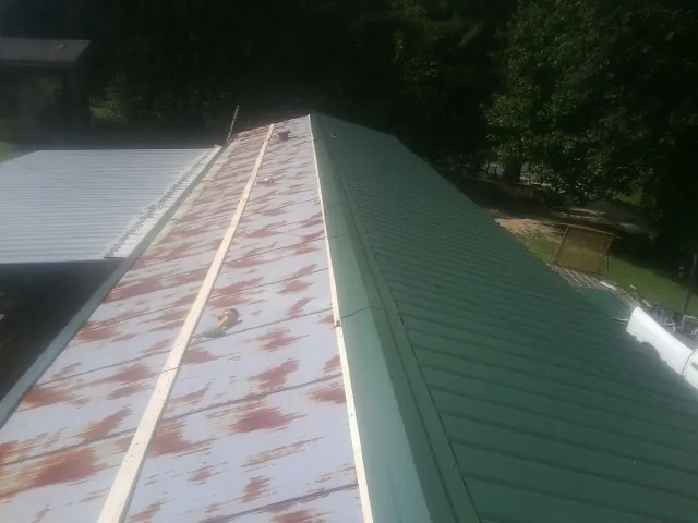 Old rusted panels beside newly installed green metal roofing — Wind Damage Roof Repair by Roofing Brothers in Little Cedar