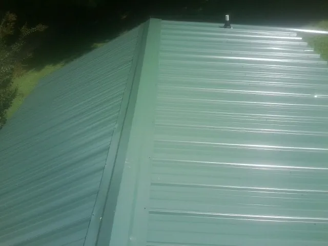 New green metal panels meeting at the ridge of a roof — Flat Roof Repair work by our crew in Little Cedar