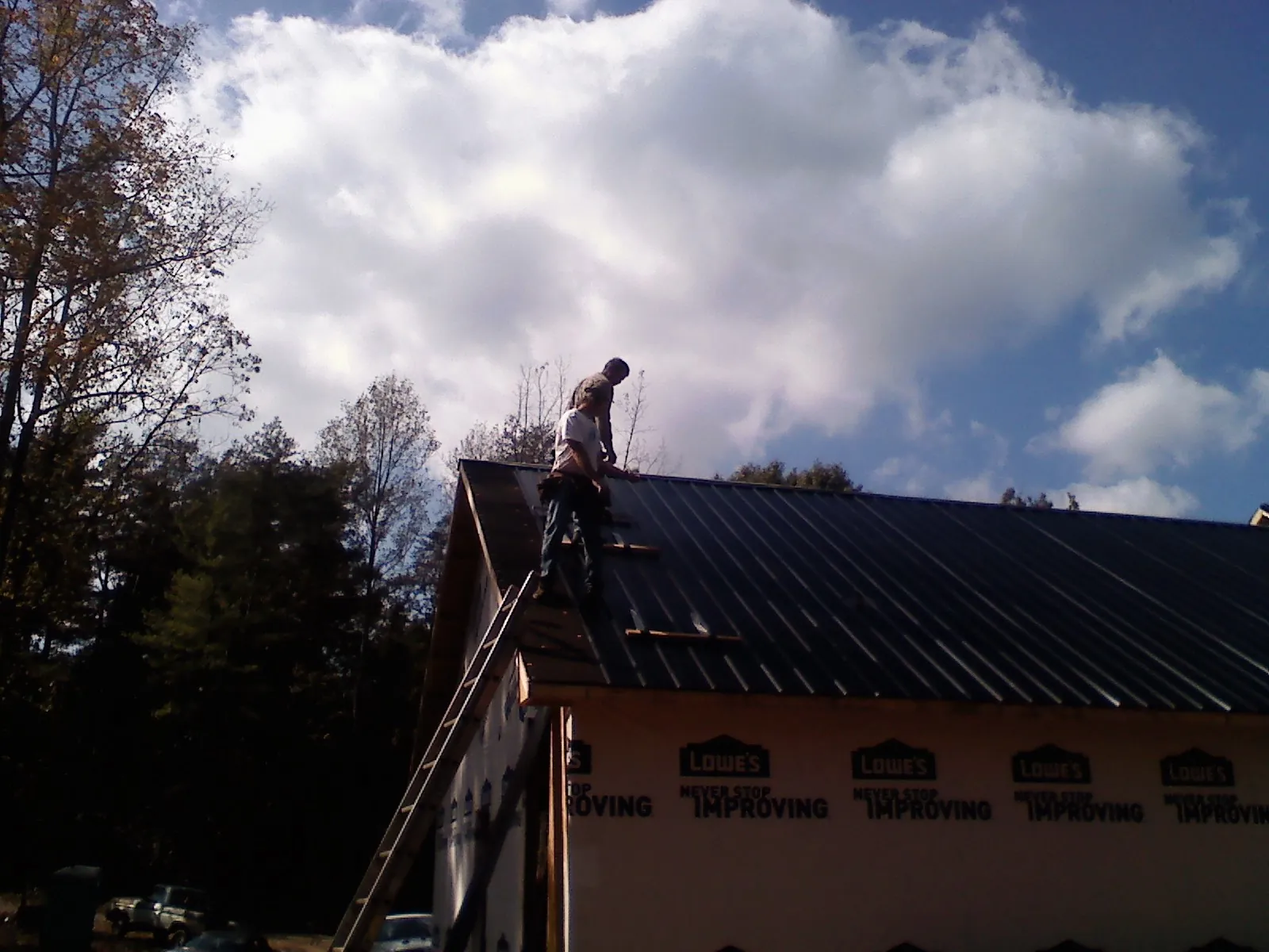 Roofer fastening dark metal panels high against a cloudy sky, from a Roof Inspection job in Little Cedar