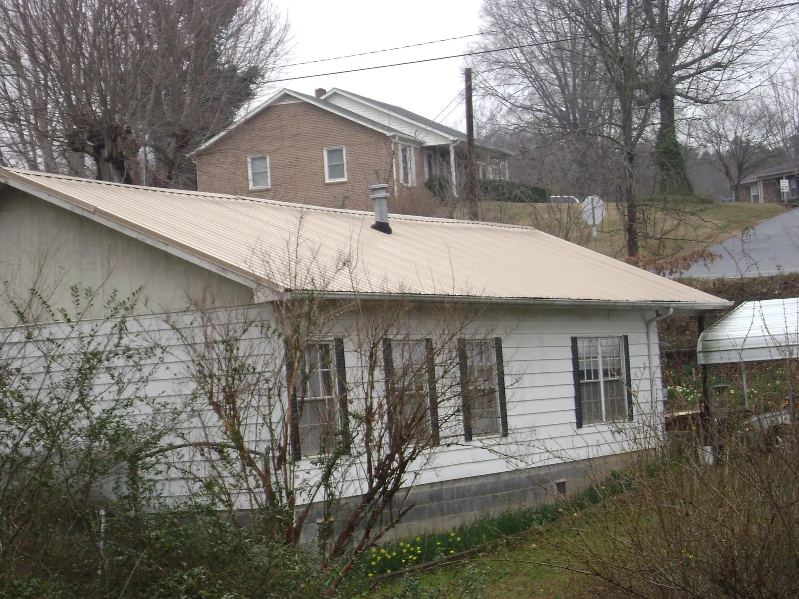 Tan metal roof on a white sided house set into a hillside — Commercial Roofing by Roofing Brothers in Little Cedar