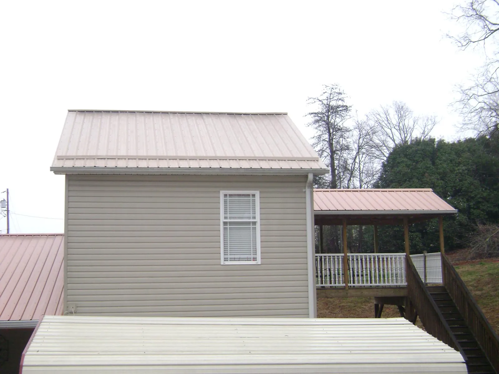 Tan metal roofs on a two story addition and attached porch, from a Roof Replacement job in Little Cedar